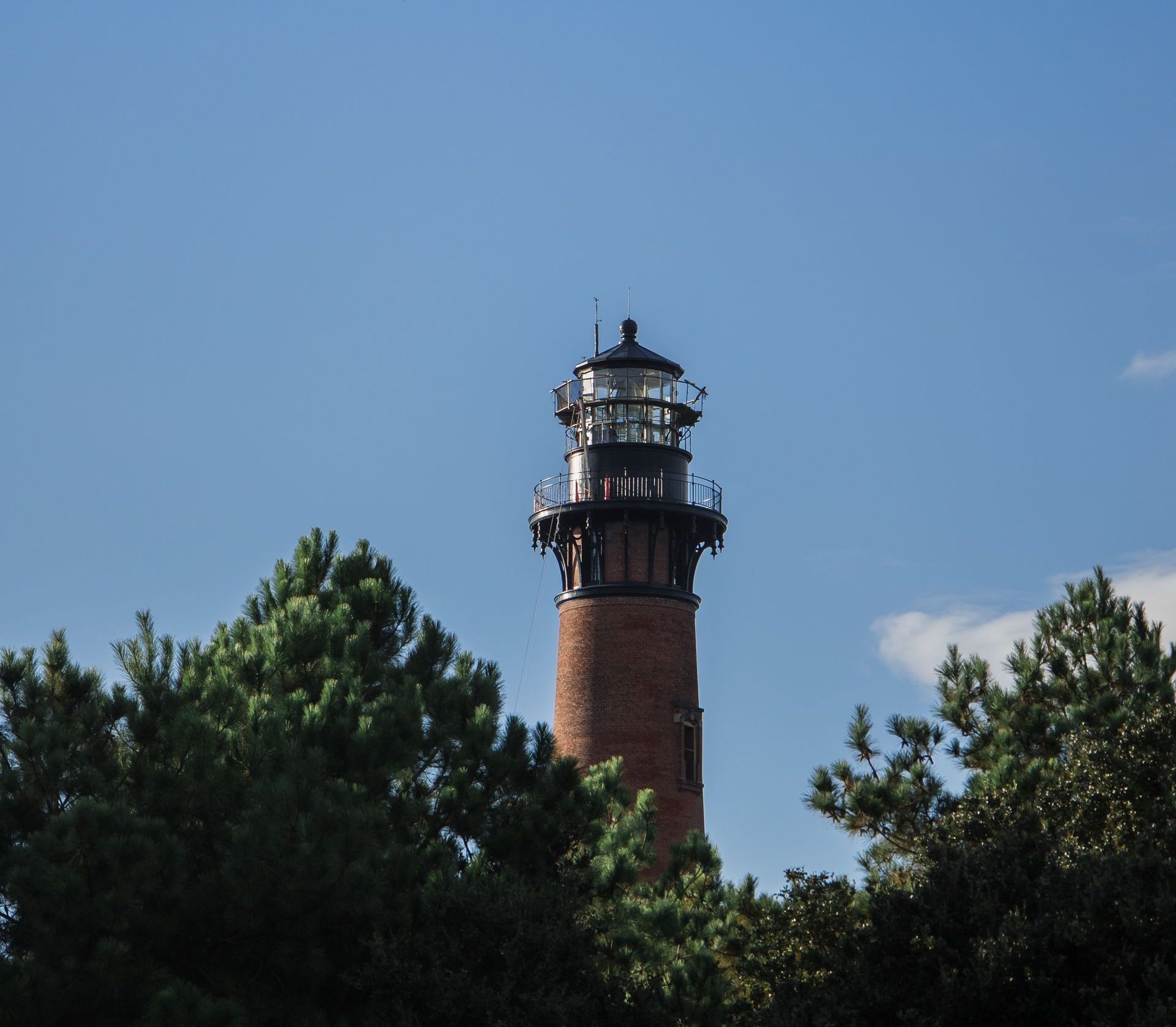 A lighthouse is surrounded by trees and a blue sky