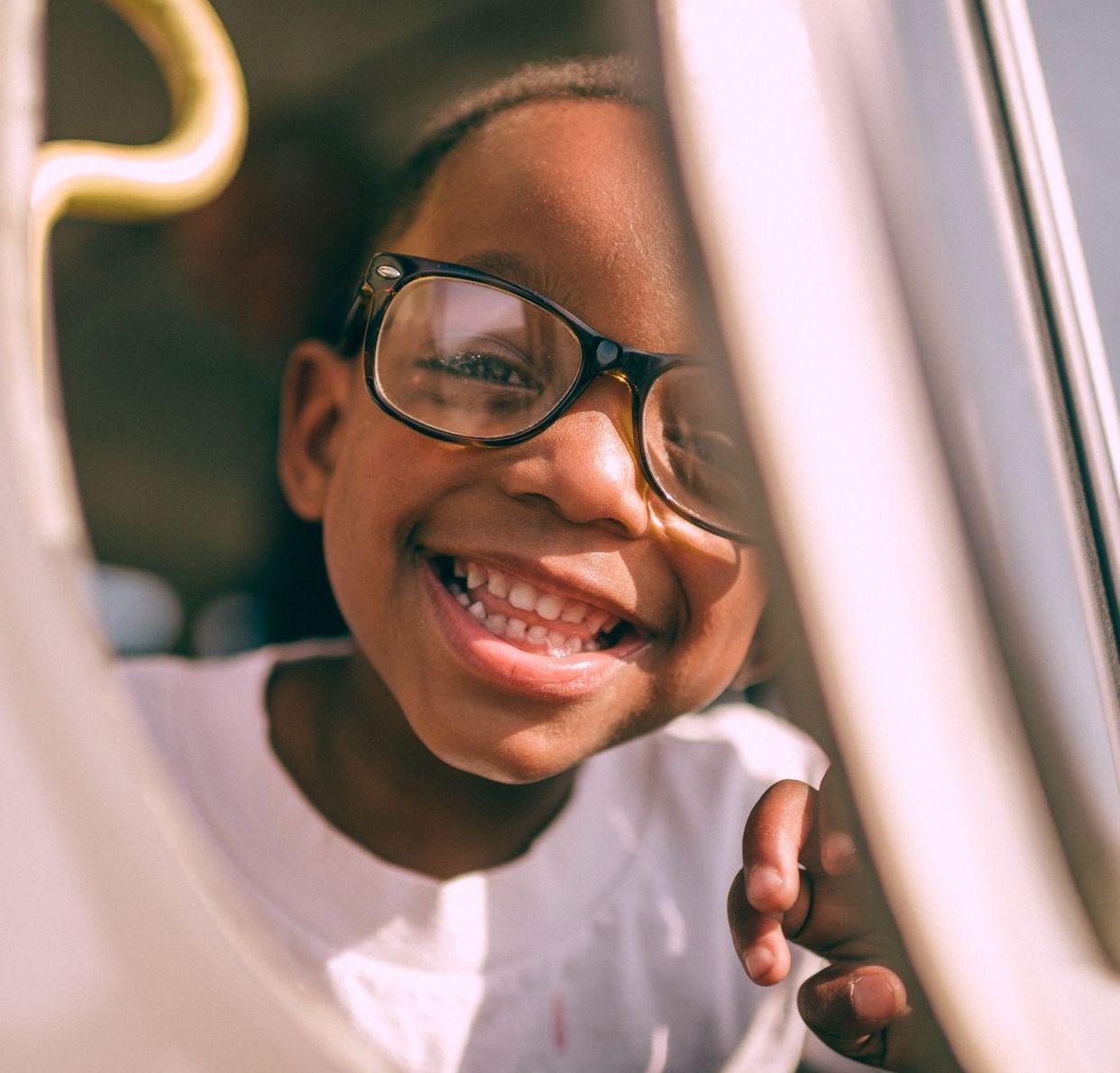 A young girl wearing glasses is smiling in a car