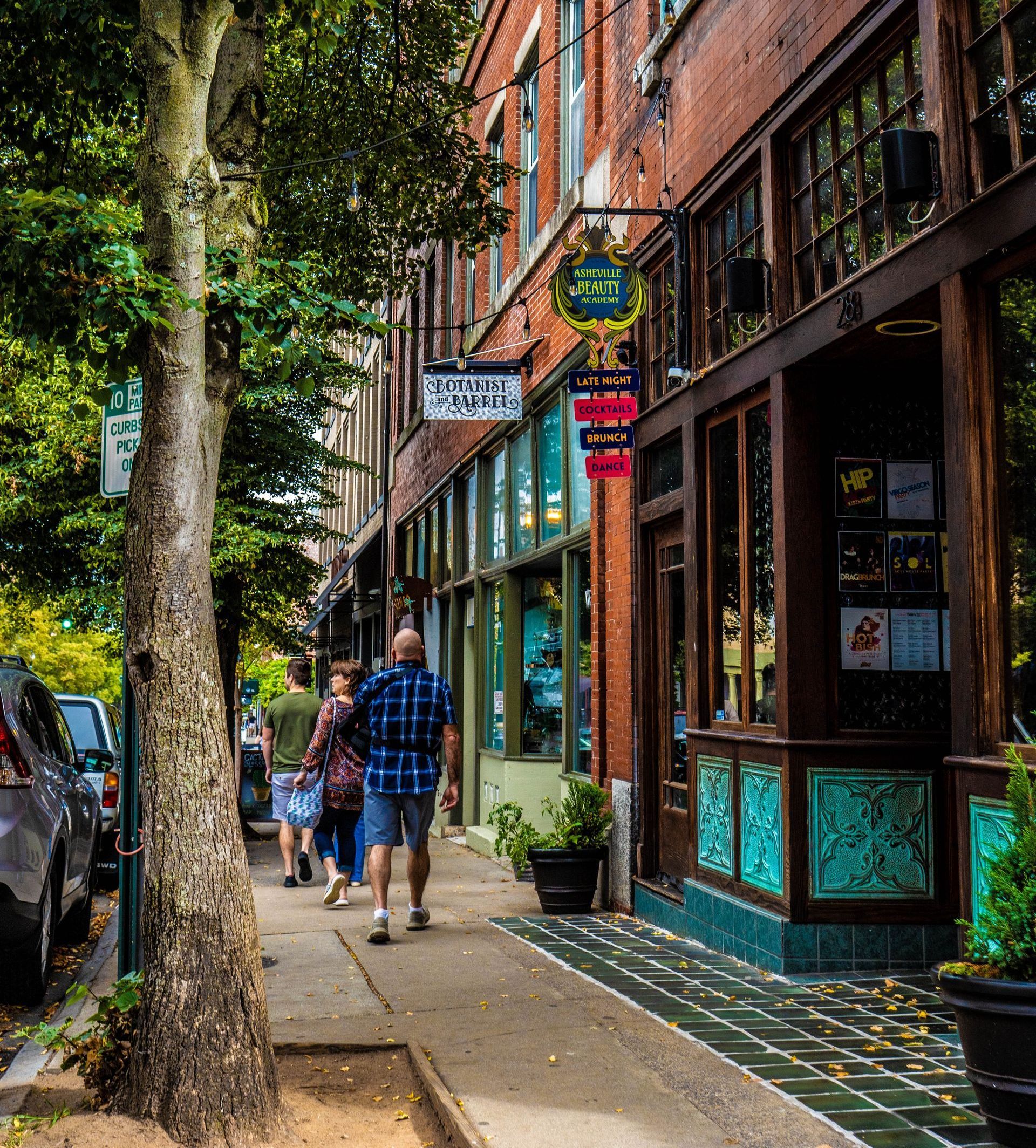 A group of people are walking down a sidewalk in front of a brick building