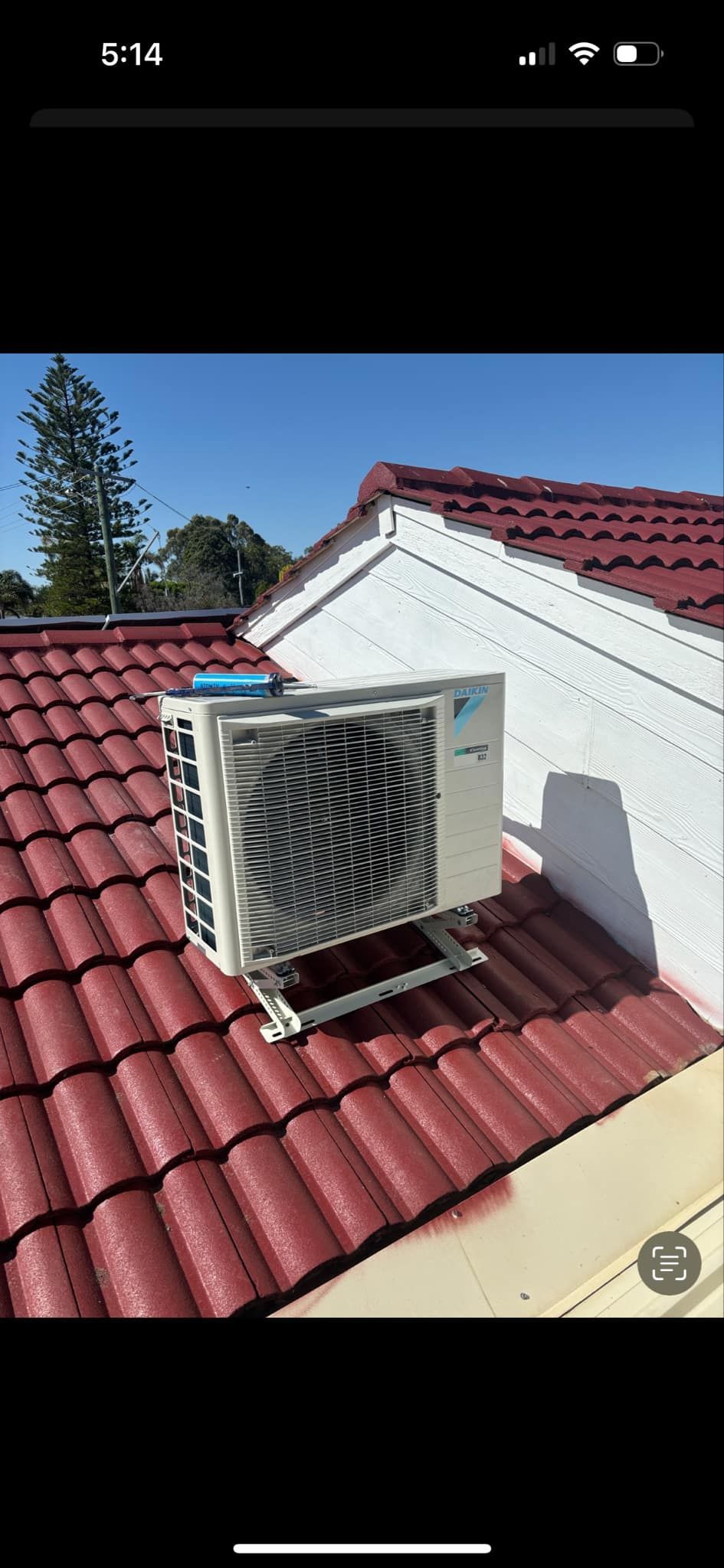 A white air conditioner is sitting on a sidewalk next to a brick wall.
