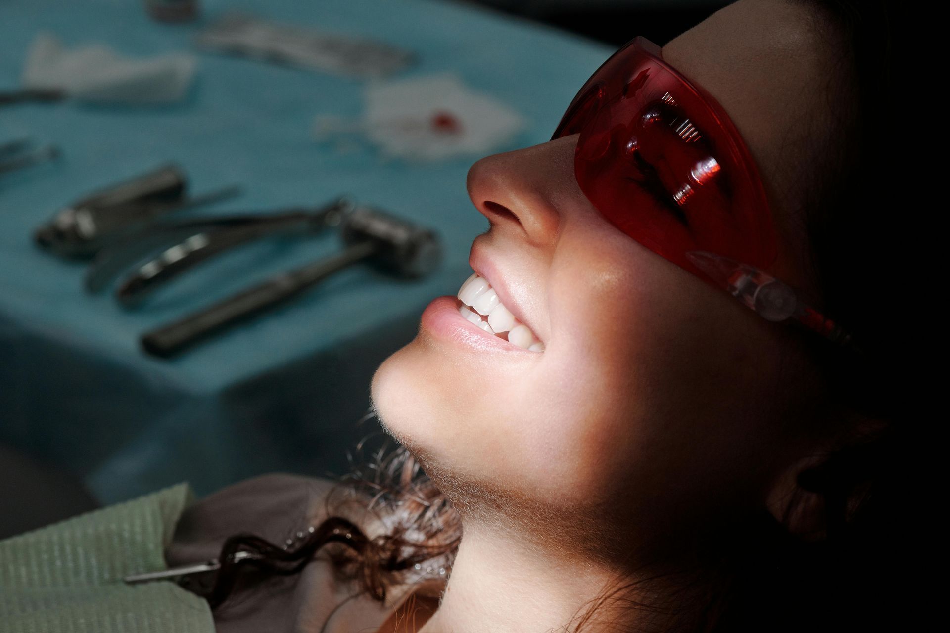 Person wearing safety glasses at the dentist, smiling with tools in the background.