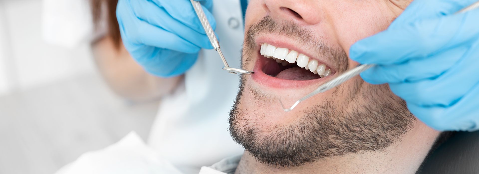 A person having a dental checkup. Dentist's gloved hands with tools in mouth.