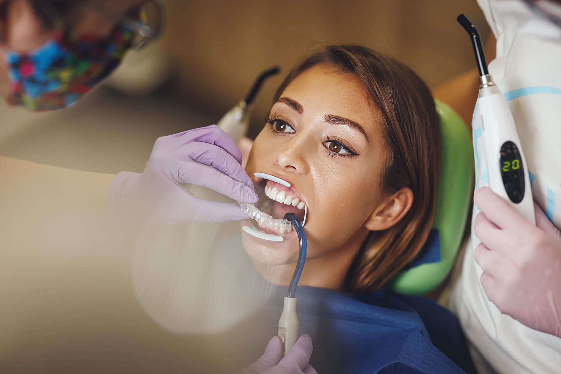 Woman at the dentist with mouth open; dental tools and assistant present.