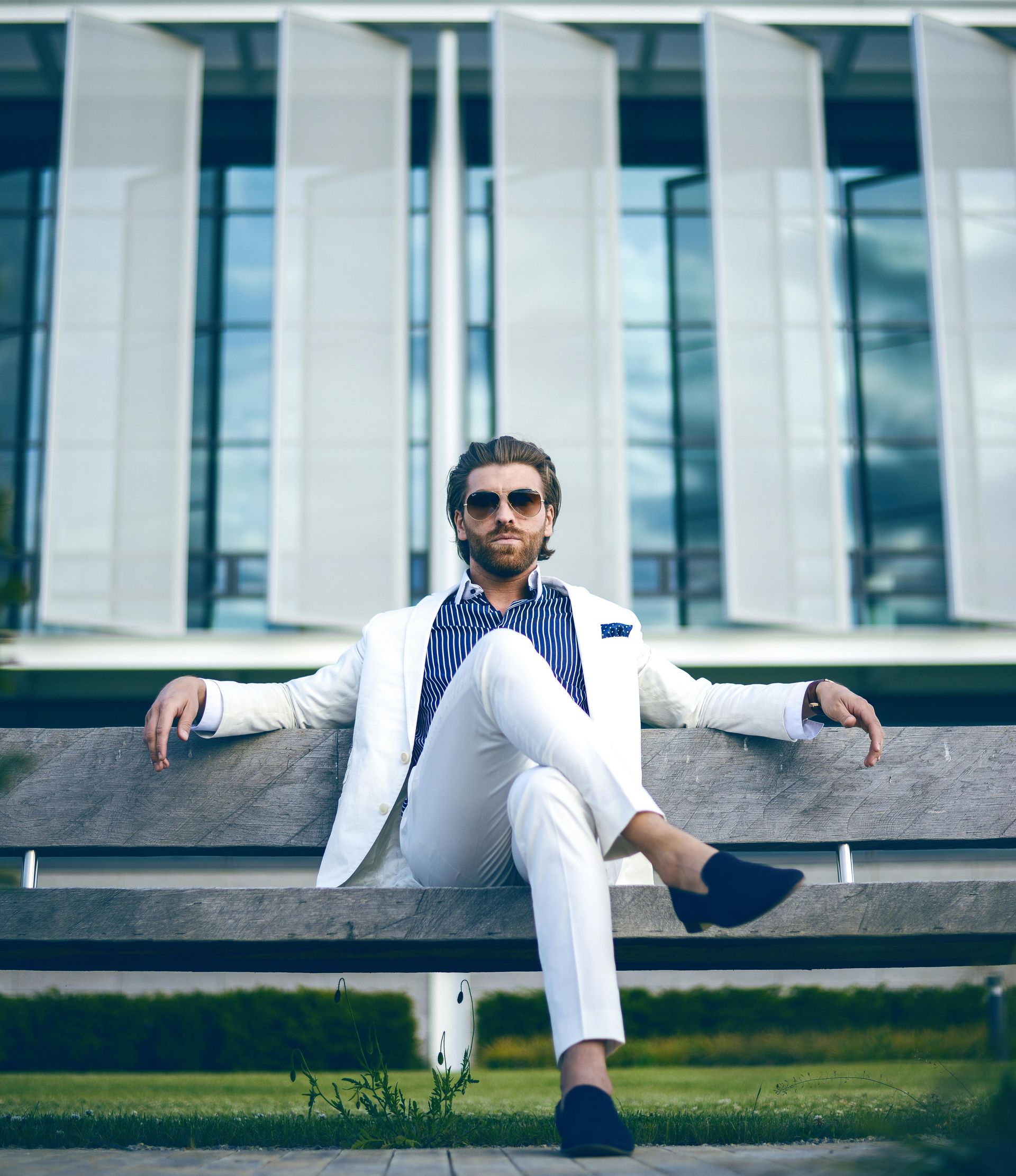 A man in a white suit is sitting on a bench with his legs crossed.