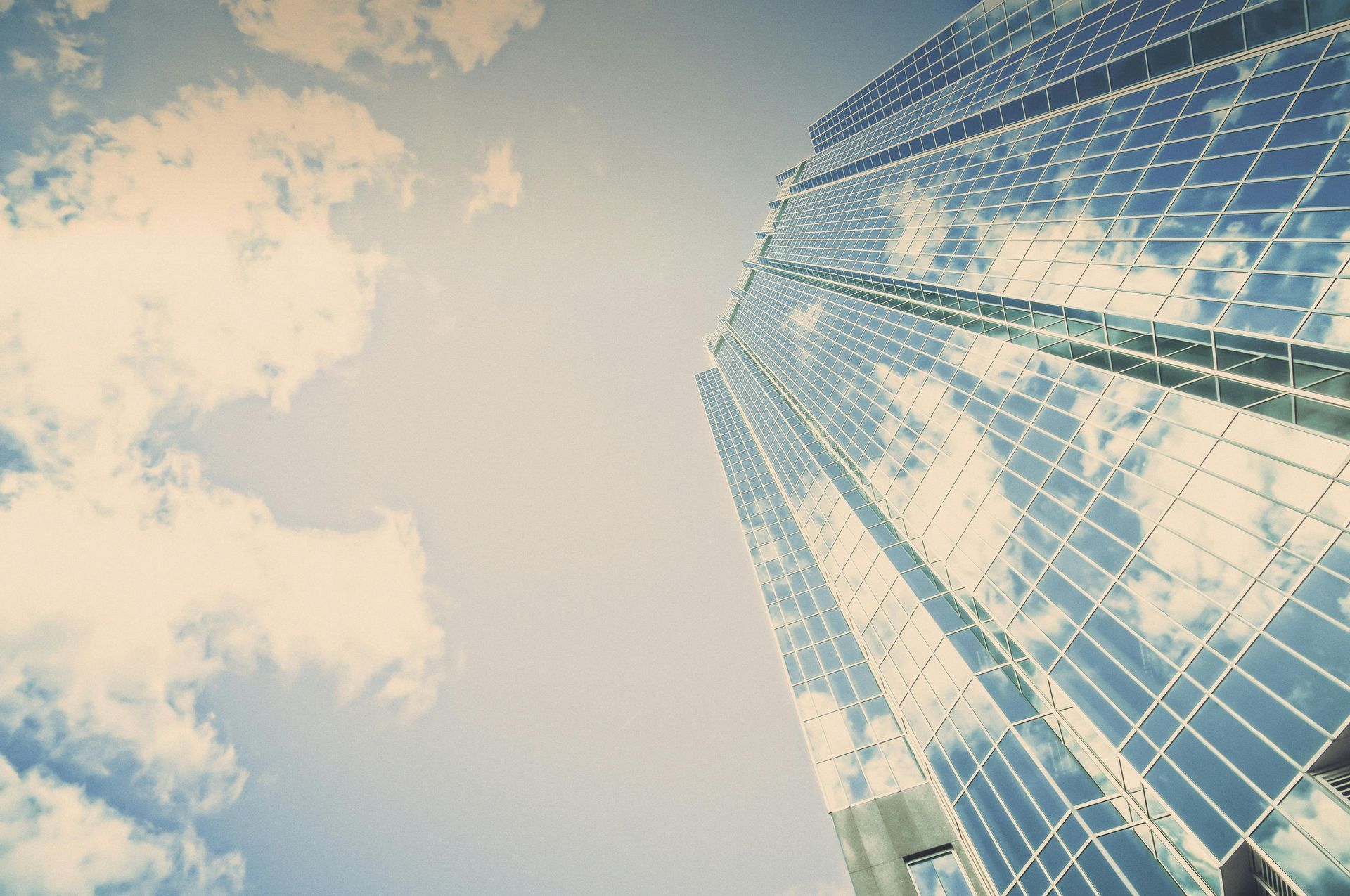 Looking up at a tall building with a blue sky and clouds reflected in the windows.