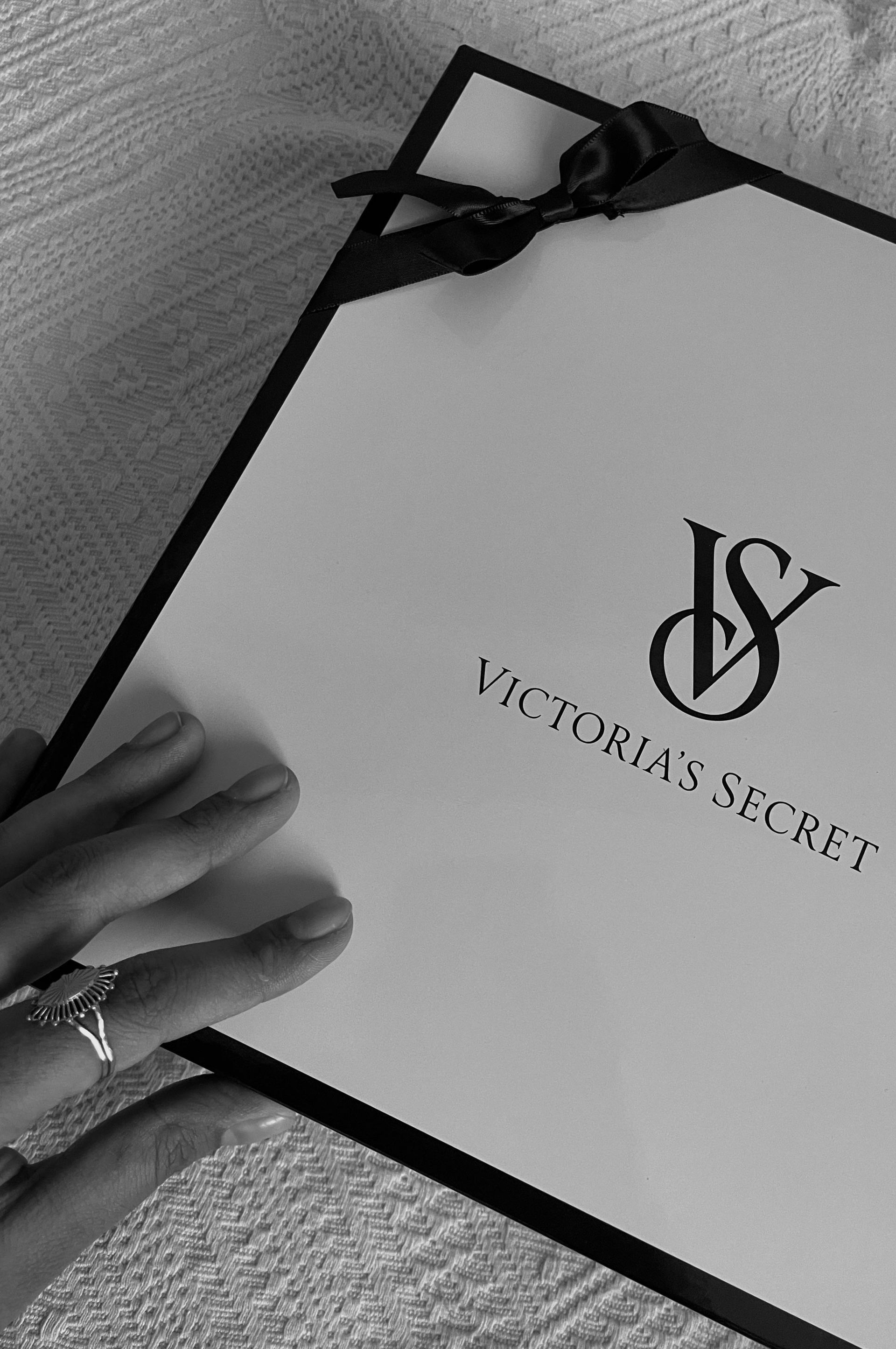 A black and white photo of a person holding a victoria 's secret gift bag