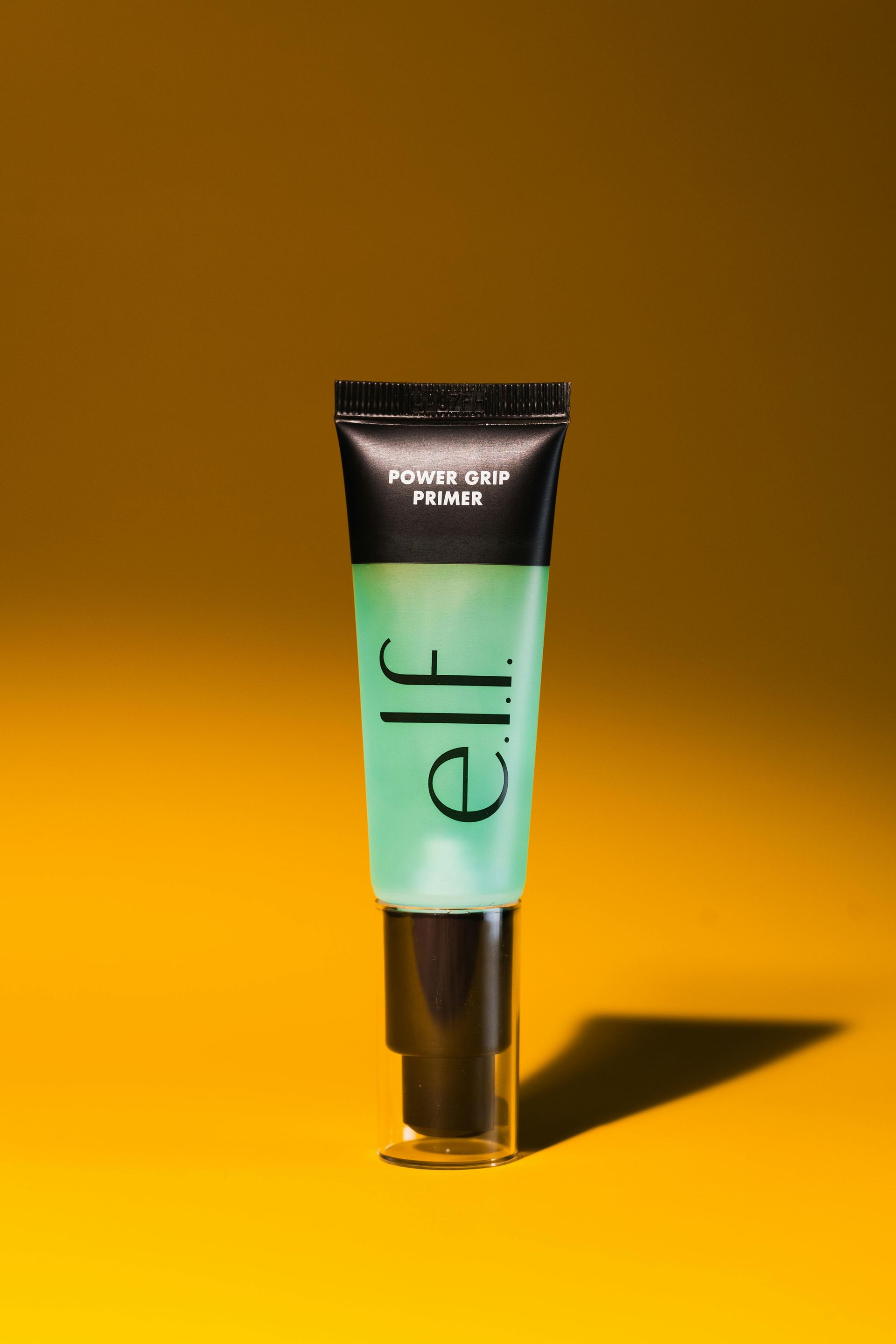 A green tube of elf makeup is sitting on a yellow surface.