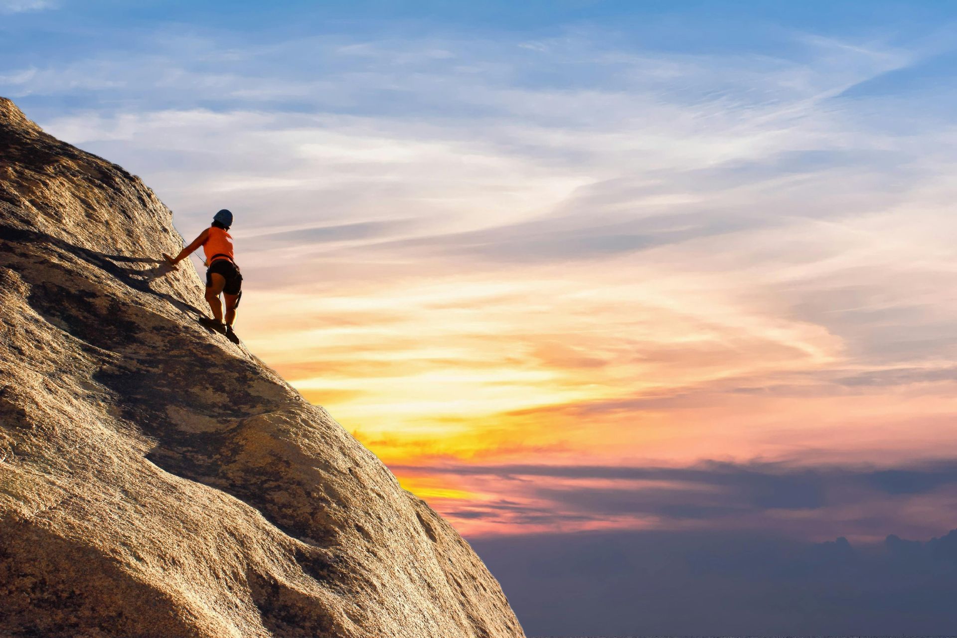 A person is climbing up the side of a mountain at sunset.