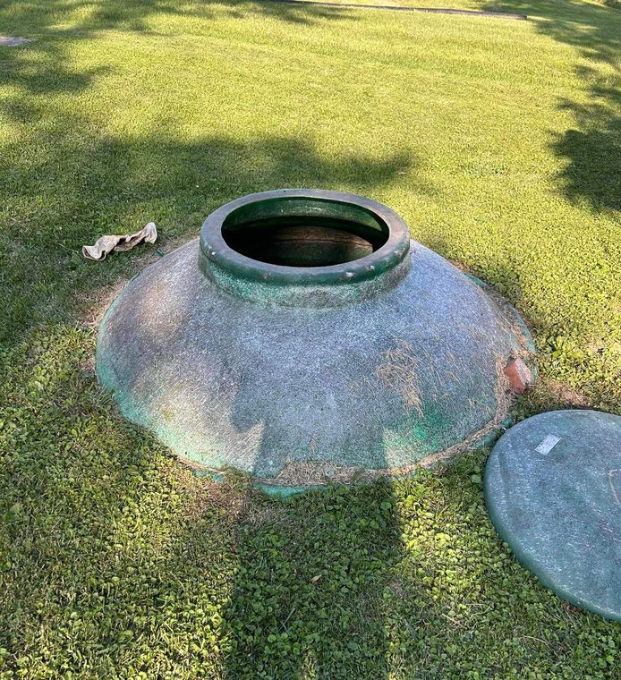 A large green container is sitting on top of a lush green field.