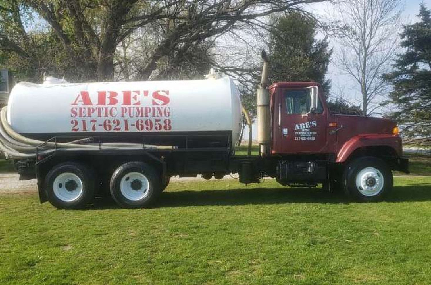 A red septic pumping truck is parked in a grassy field.