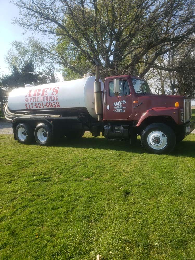 A red and white septic tank truck is parked in a grassy field.