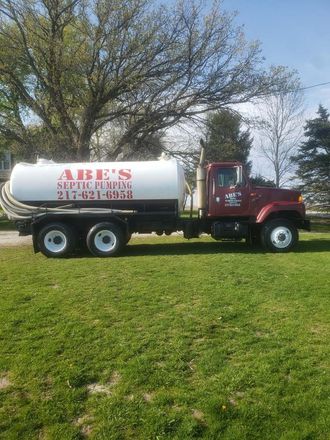 A red and white septic truck is parked in a grassy field.