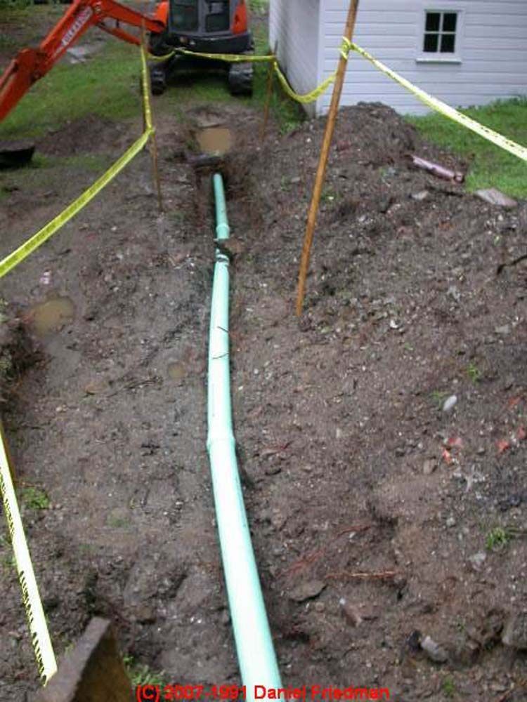A green pipe is being installed in the dirt next to a house.