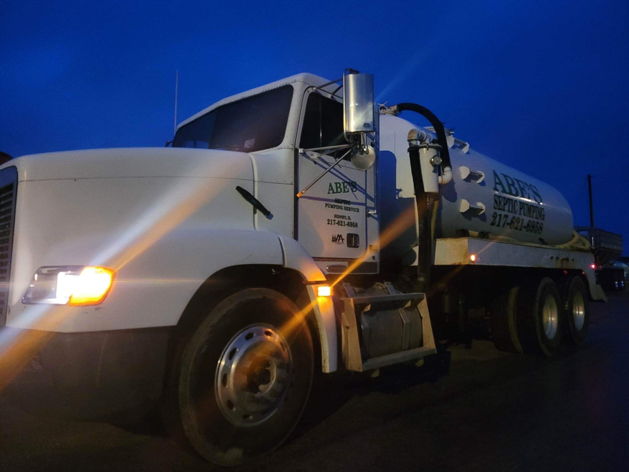 A white vacuum truck is parked in a parking lot at night