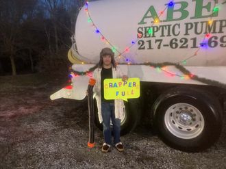 A man is standing in front of a septic pump truck holding a sign that says rapper full.