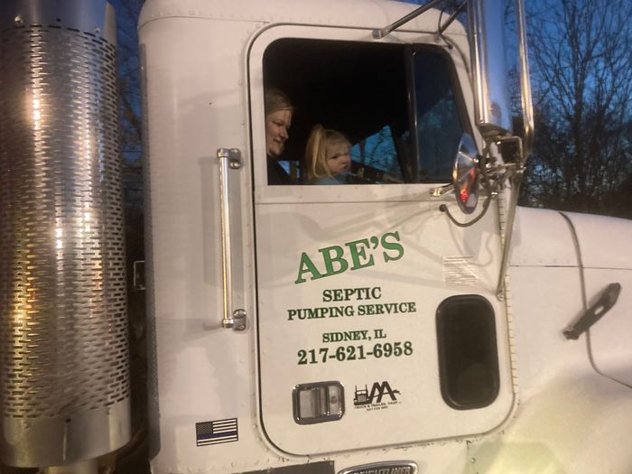 Two children are sitting in the cab of a septic pumping service truck