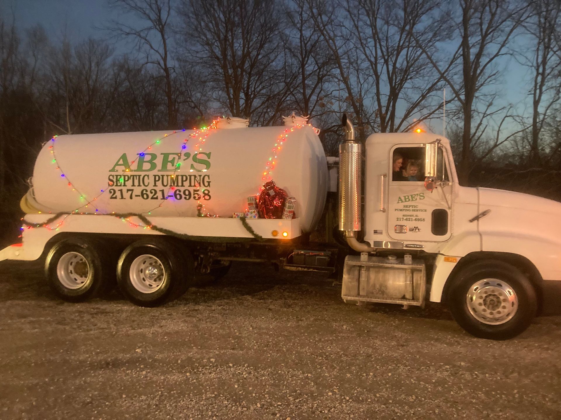 A white septic pumping truck is decorated with christmas lights.