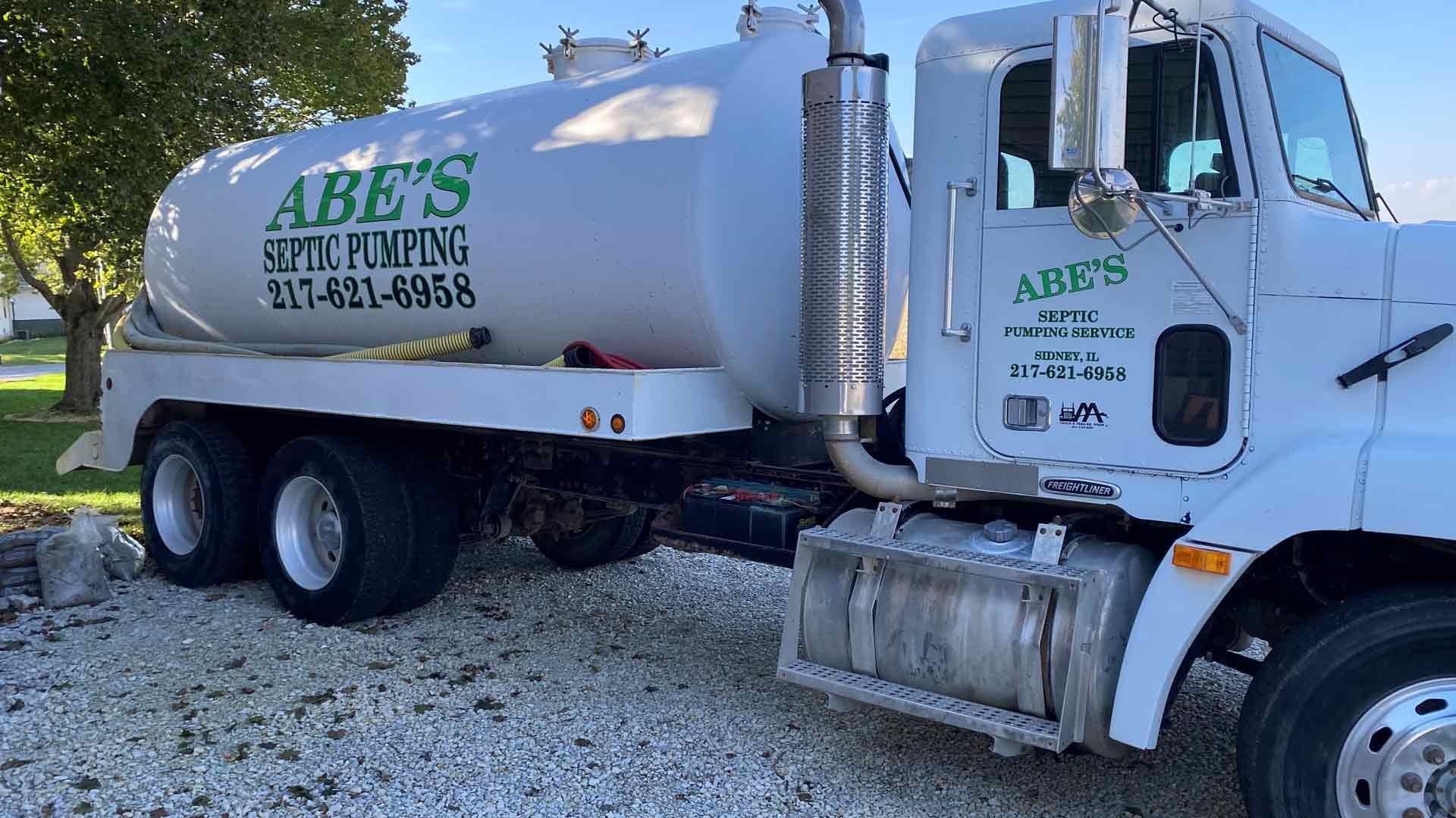 A white septic pumping truck is parked in a gravel lot.