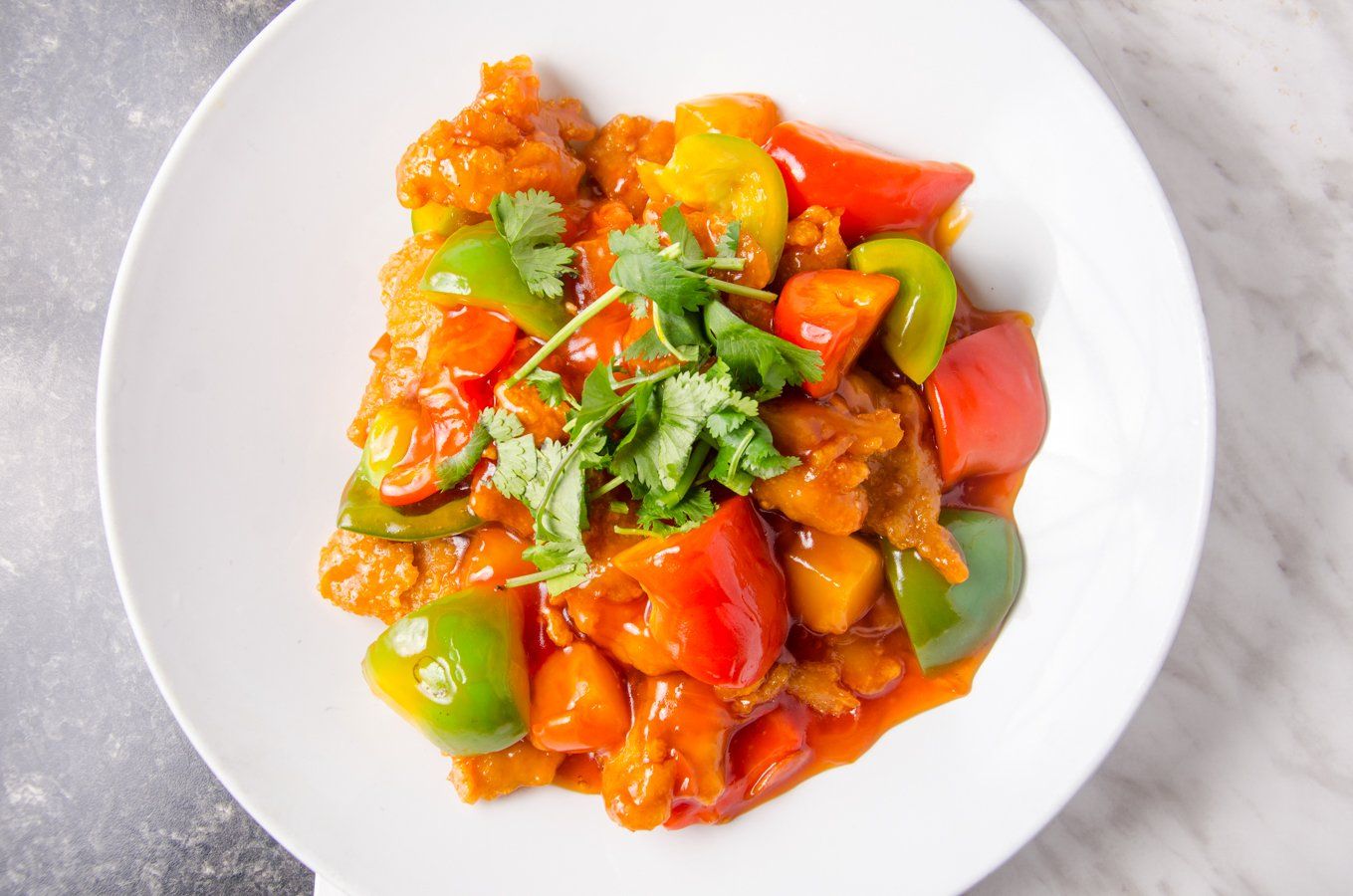 Sweet and sour chicken dish with bell peppers and cilantro on a white plate.