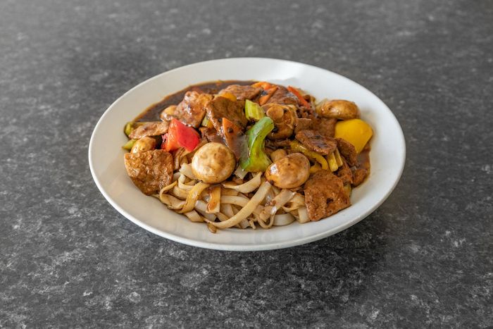Plate of stir-fry noodles with meat, mushrooms, and colorful peppers in a dark sauce.