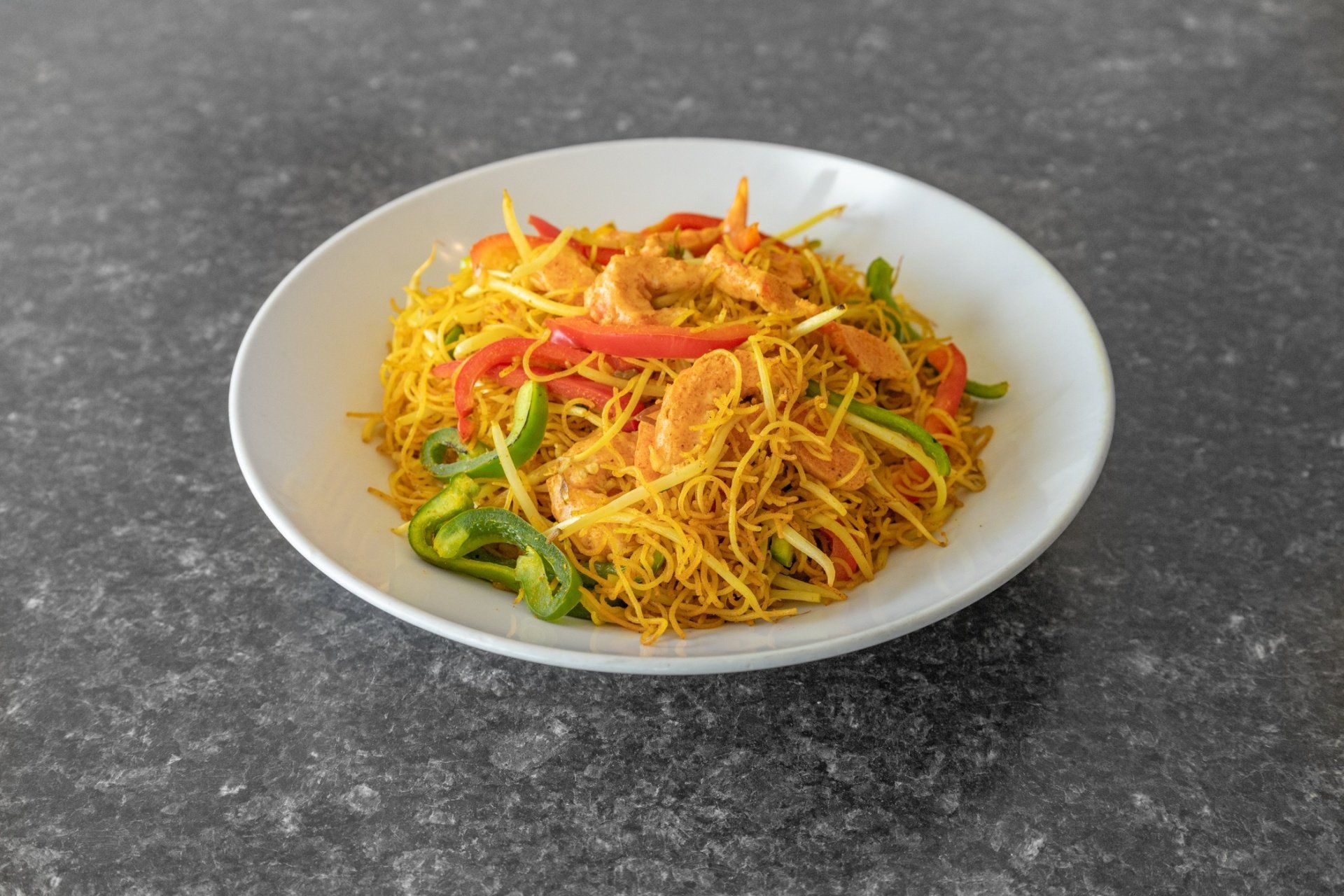 White plate of stir-fried rice noodles with shrimp, red and green peppers.