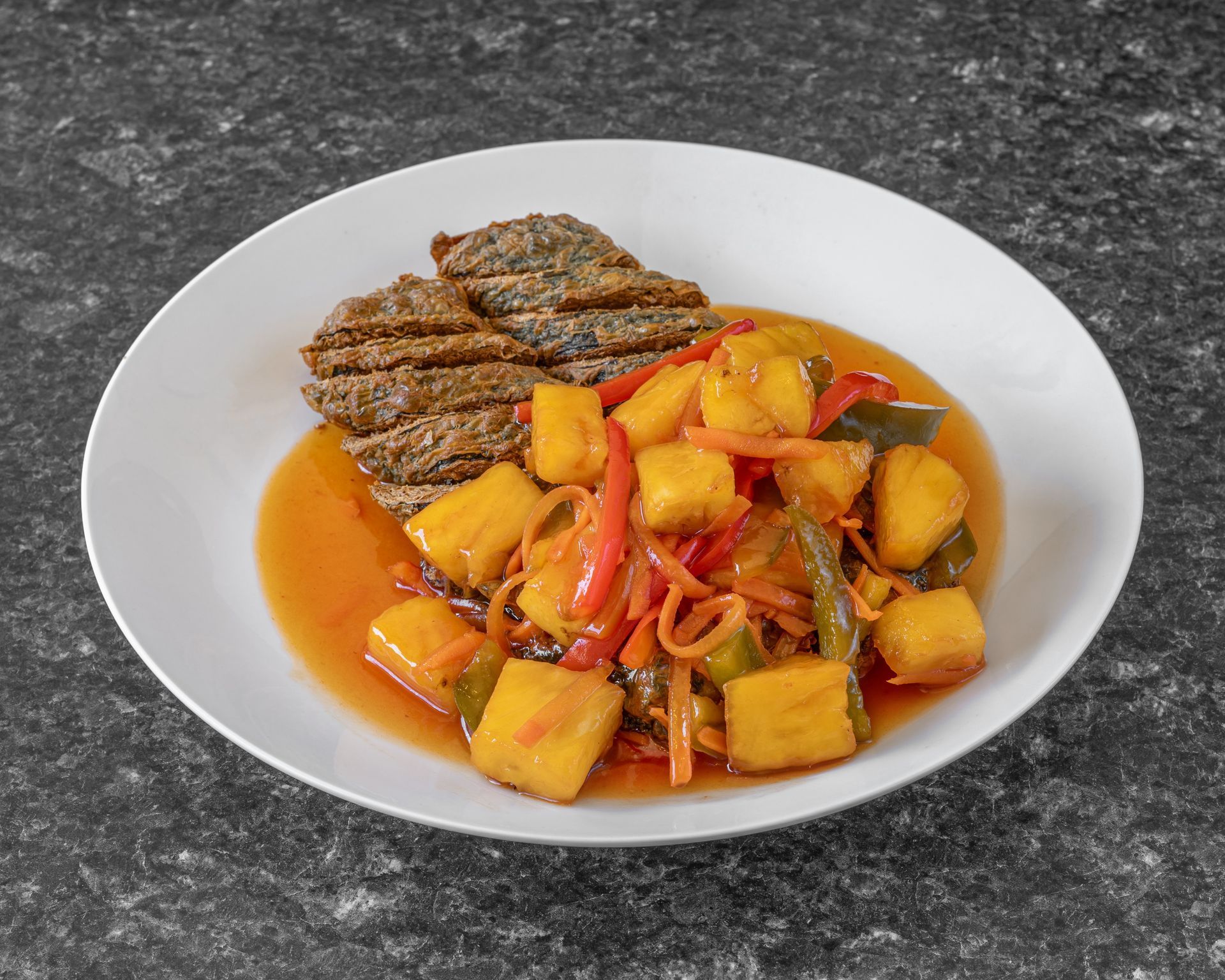 Fried fish with sweet and sour pineapple, peppers, and carrots on a white plate.