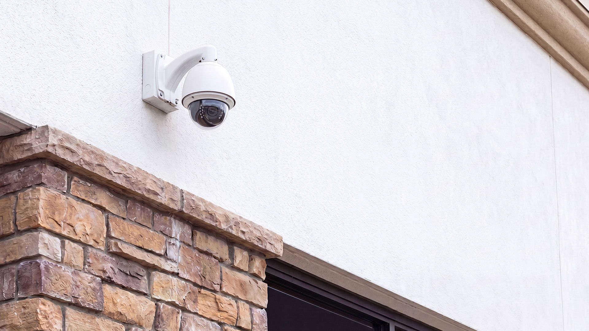 Wall-mounted security camera above a brick-and-white building facade.