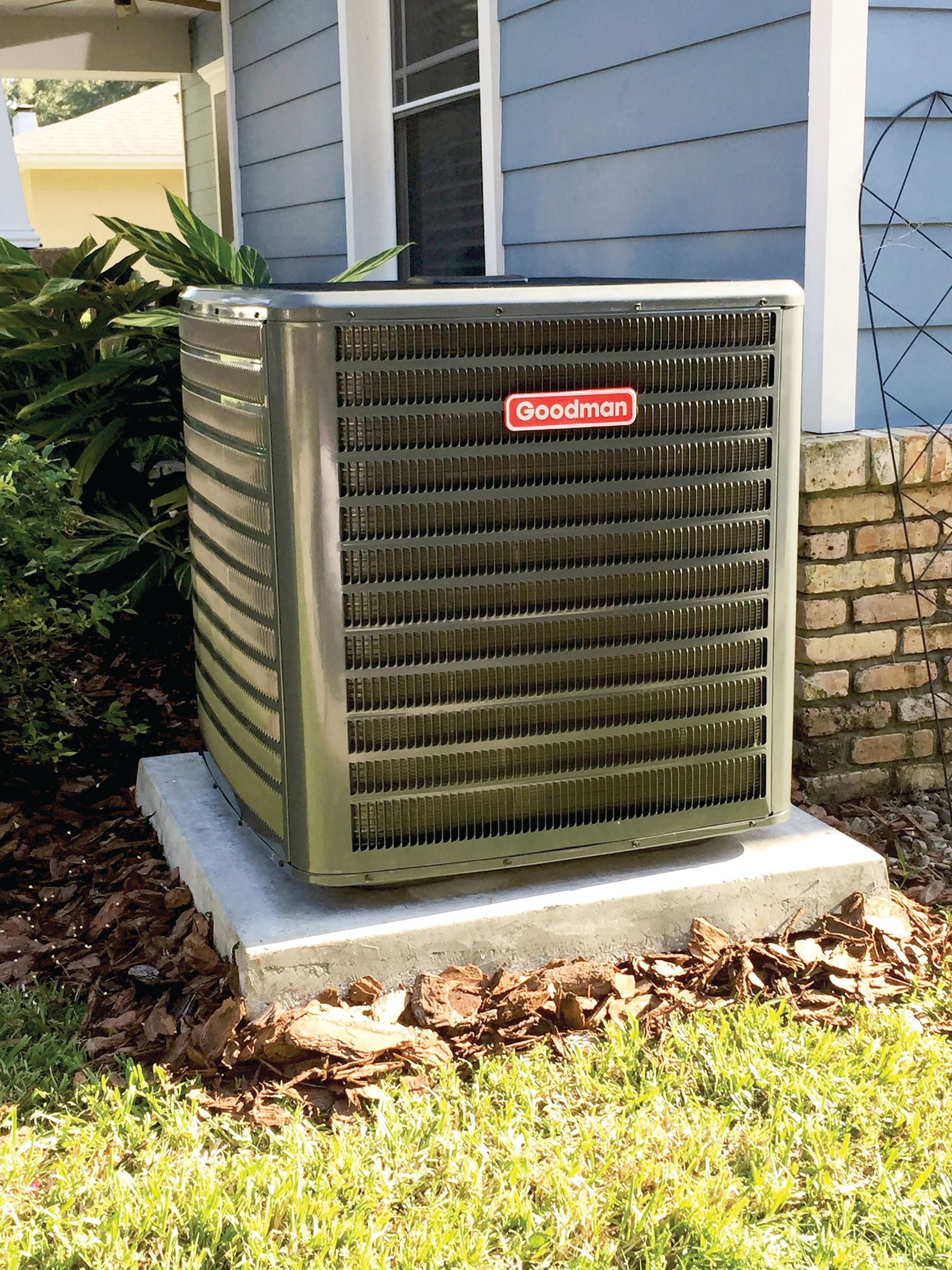 Outdoor HVAC unit beside a house, with gray metal siding and a red logo.