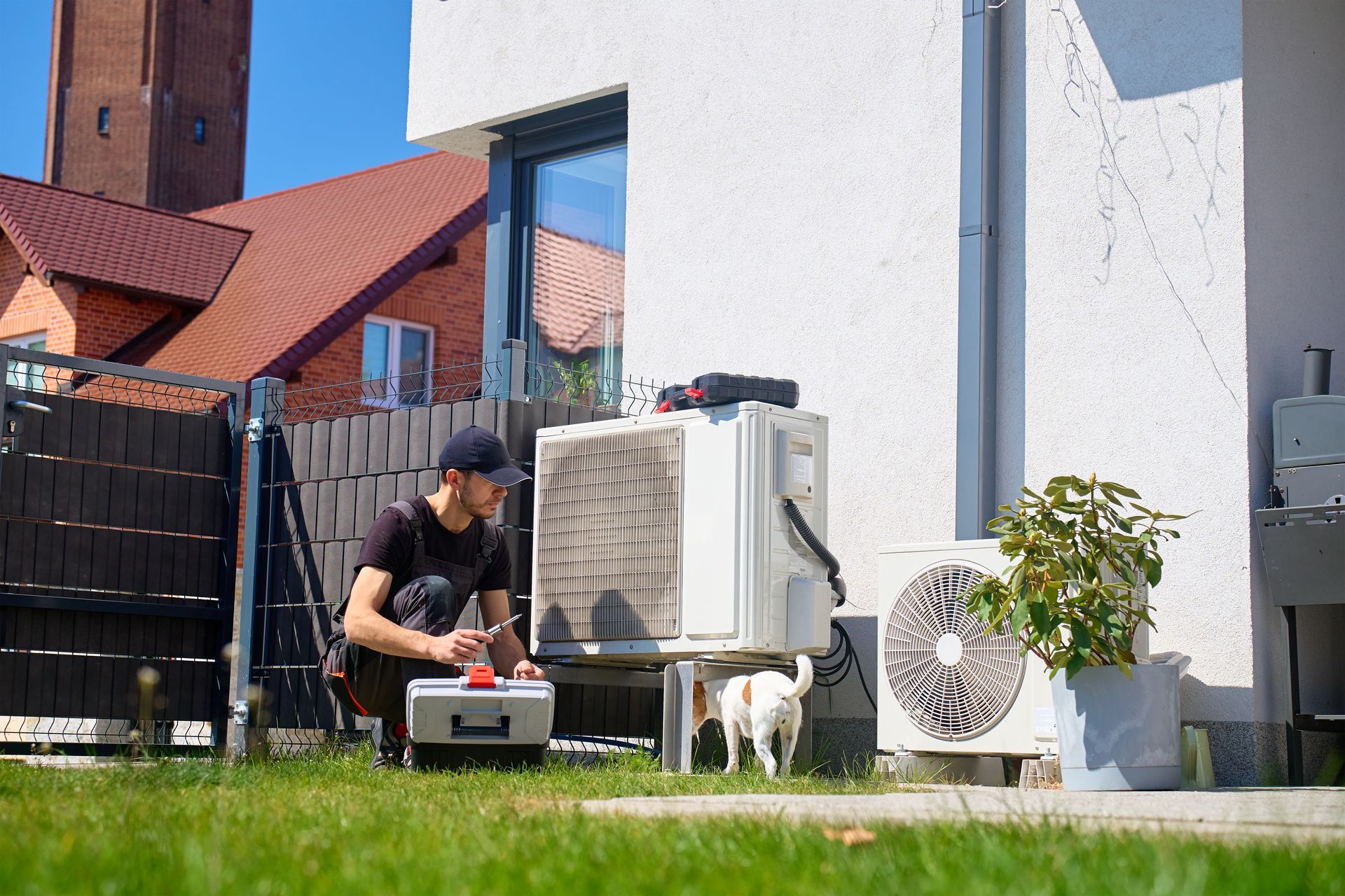 Person kneeling by outdoor AC units and a dog in a grassy backyard beside a house