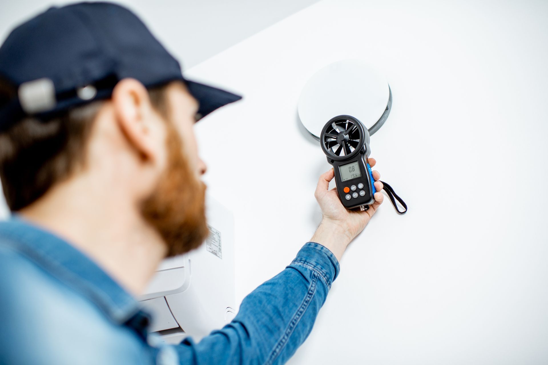 Person using anemometer to measure airflow near a ventilation outlet.