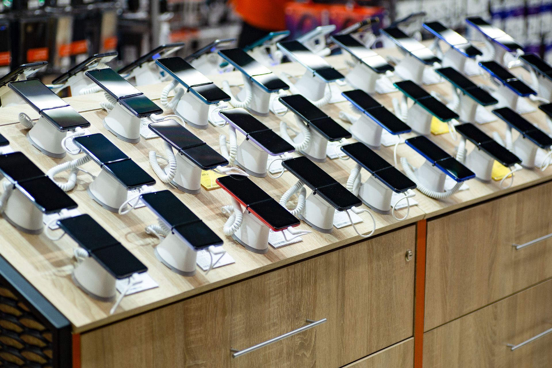 Fila de teléfonos inteligentes exhibidos en una tienda sobre soportes blancos en ángulo; gabinete de madera debajo.