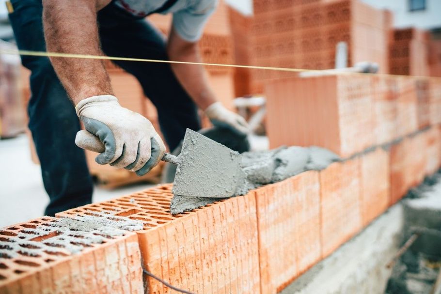 Gloved worker laying wet cement on a brick wall at a construction site