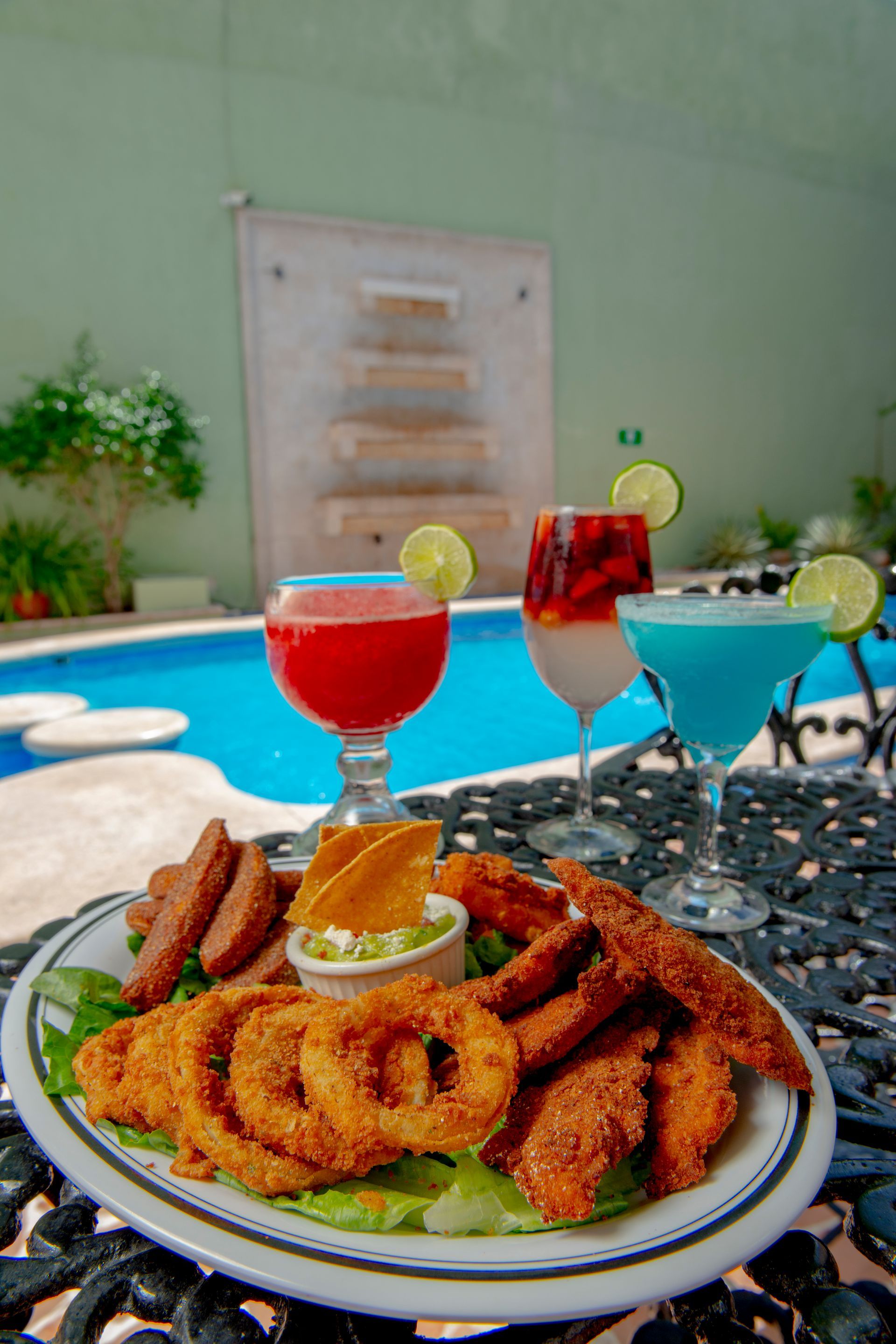 A plate of food and two drinks on a table in front of a pool.