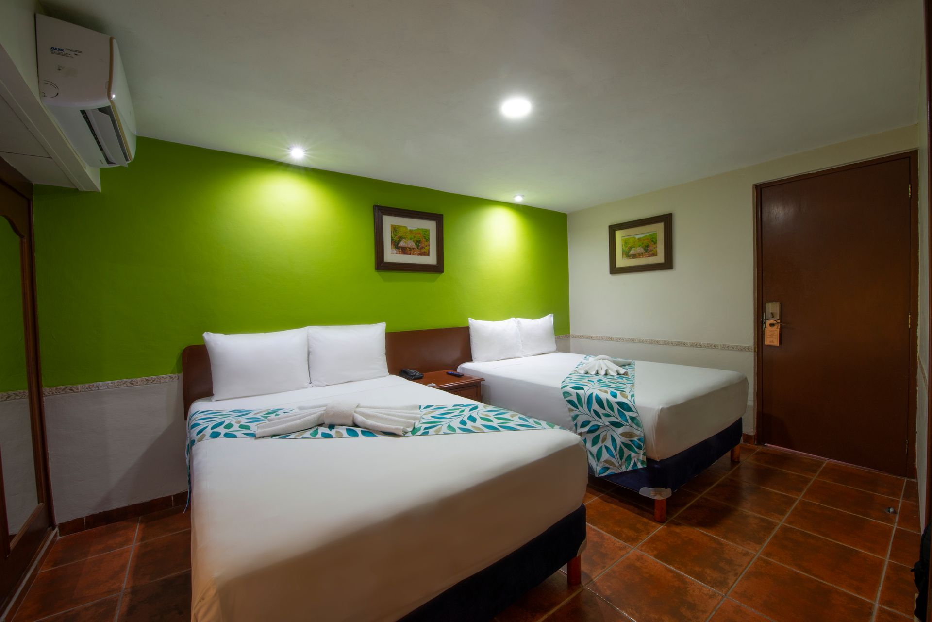 A hotel room with two beds and a green wall.
