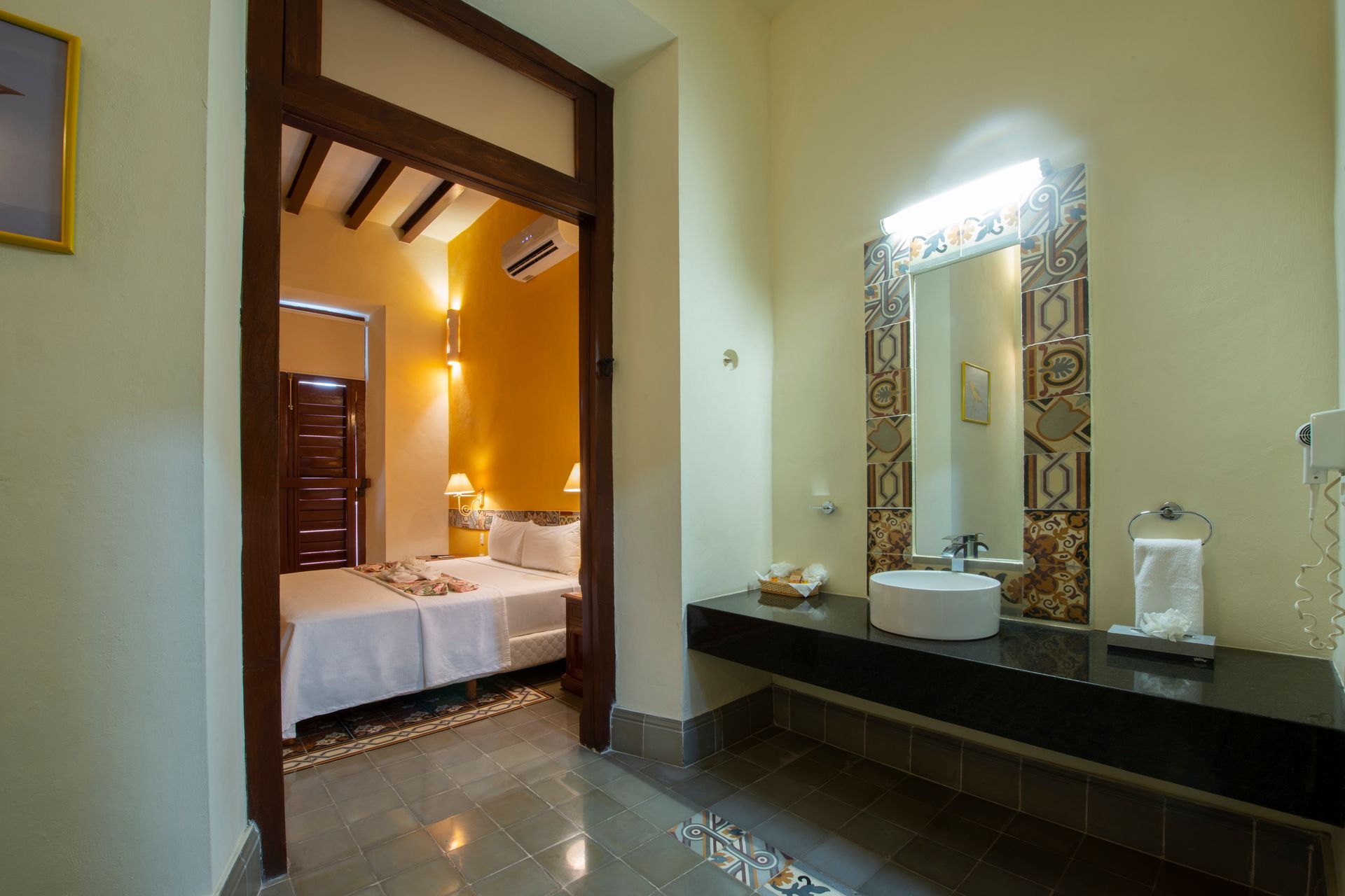 A bathroom with a sink and mirror next to a bedroom.