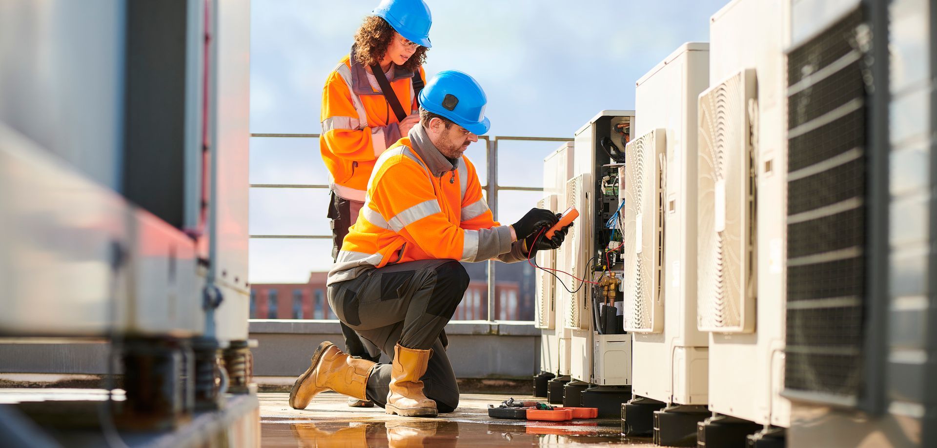 Technicians in orange uniforms, performing commercial AC system installation of several units.