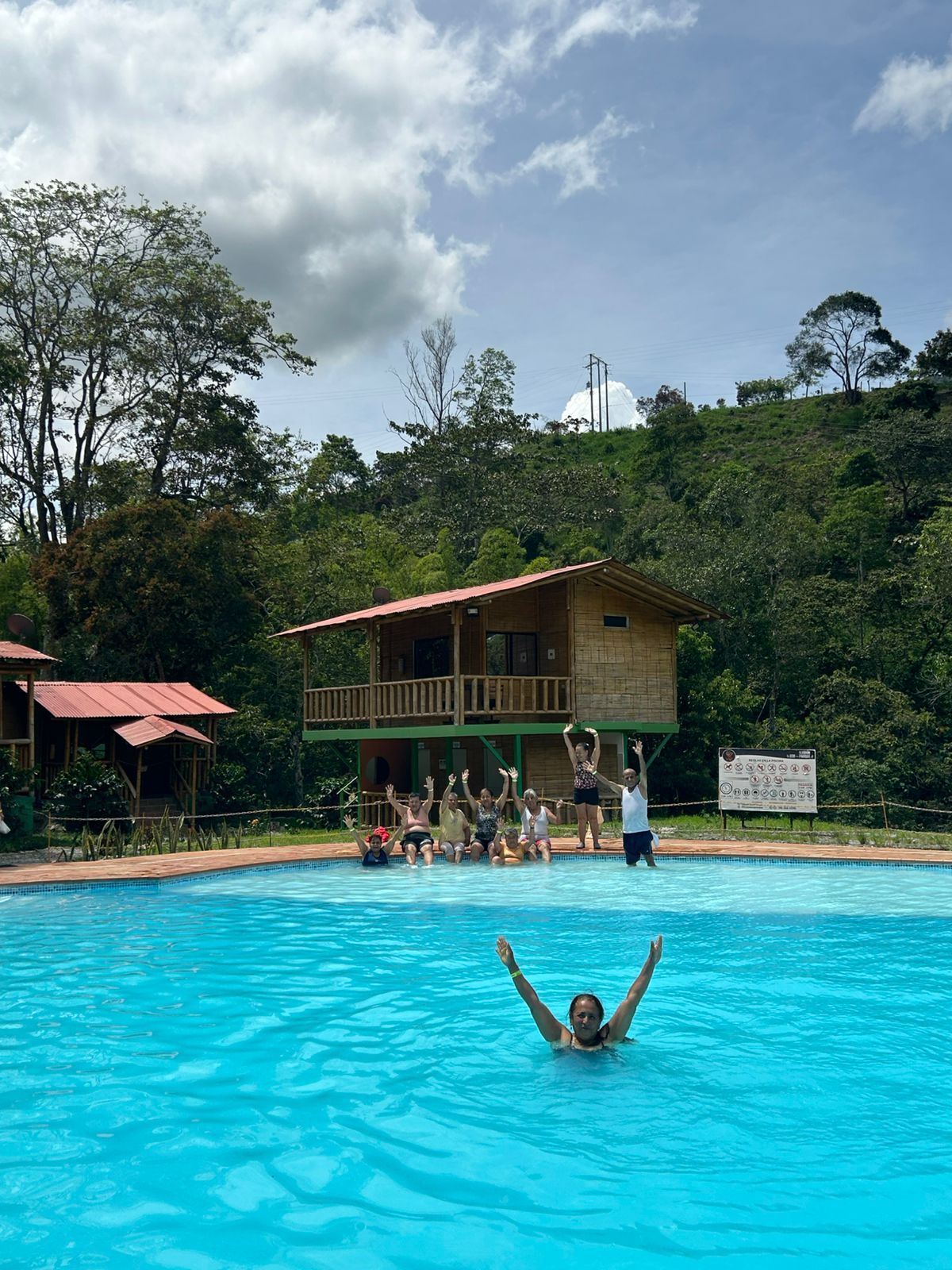 Piscina en el complejo, exuberantes montañas verdes al fondo, cielo nublado.