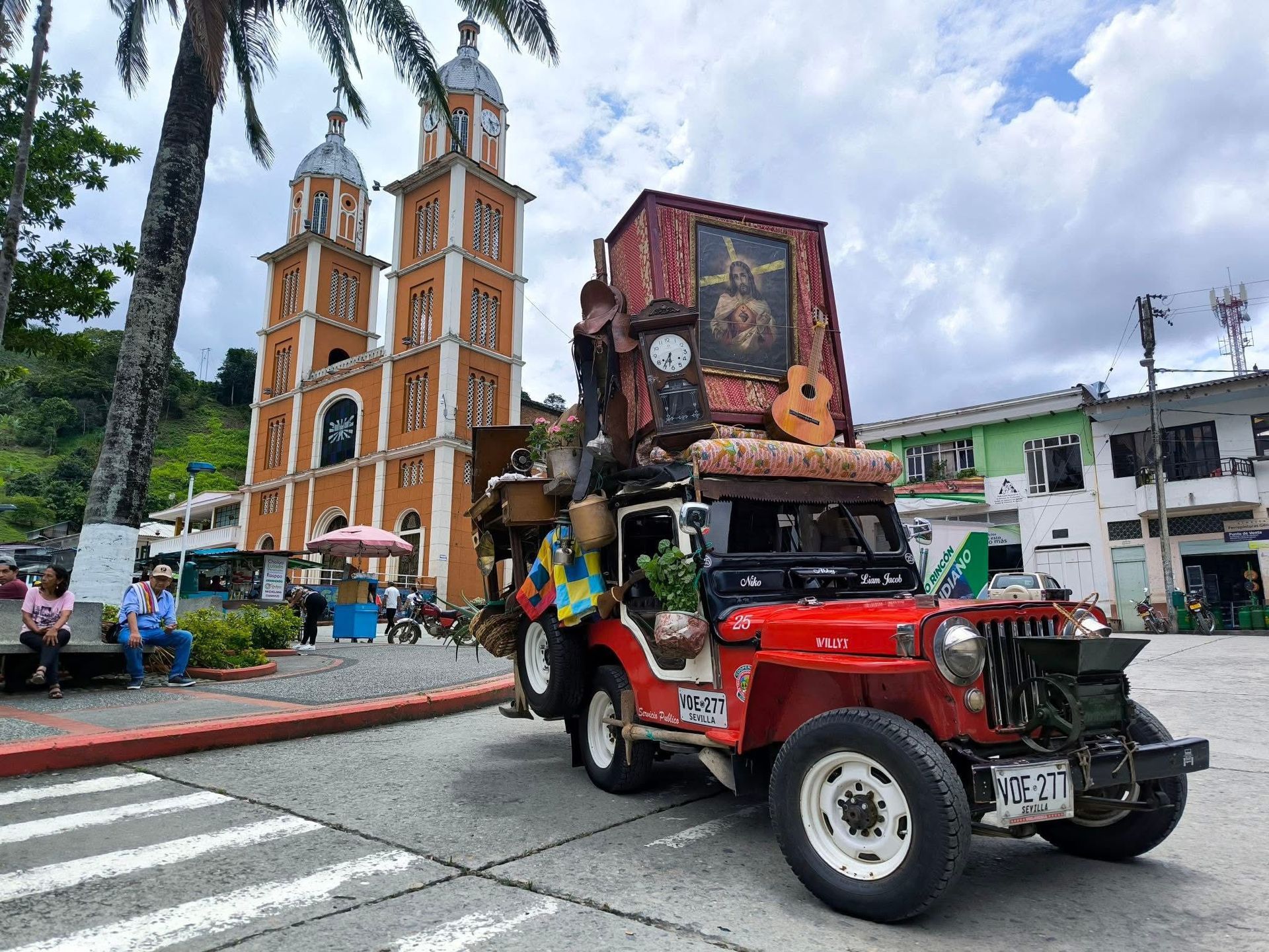 Jeep rojo cargado de artículos frente a una iglesia naranja.