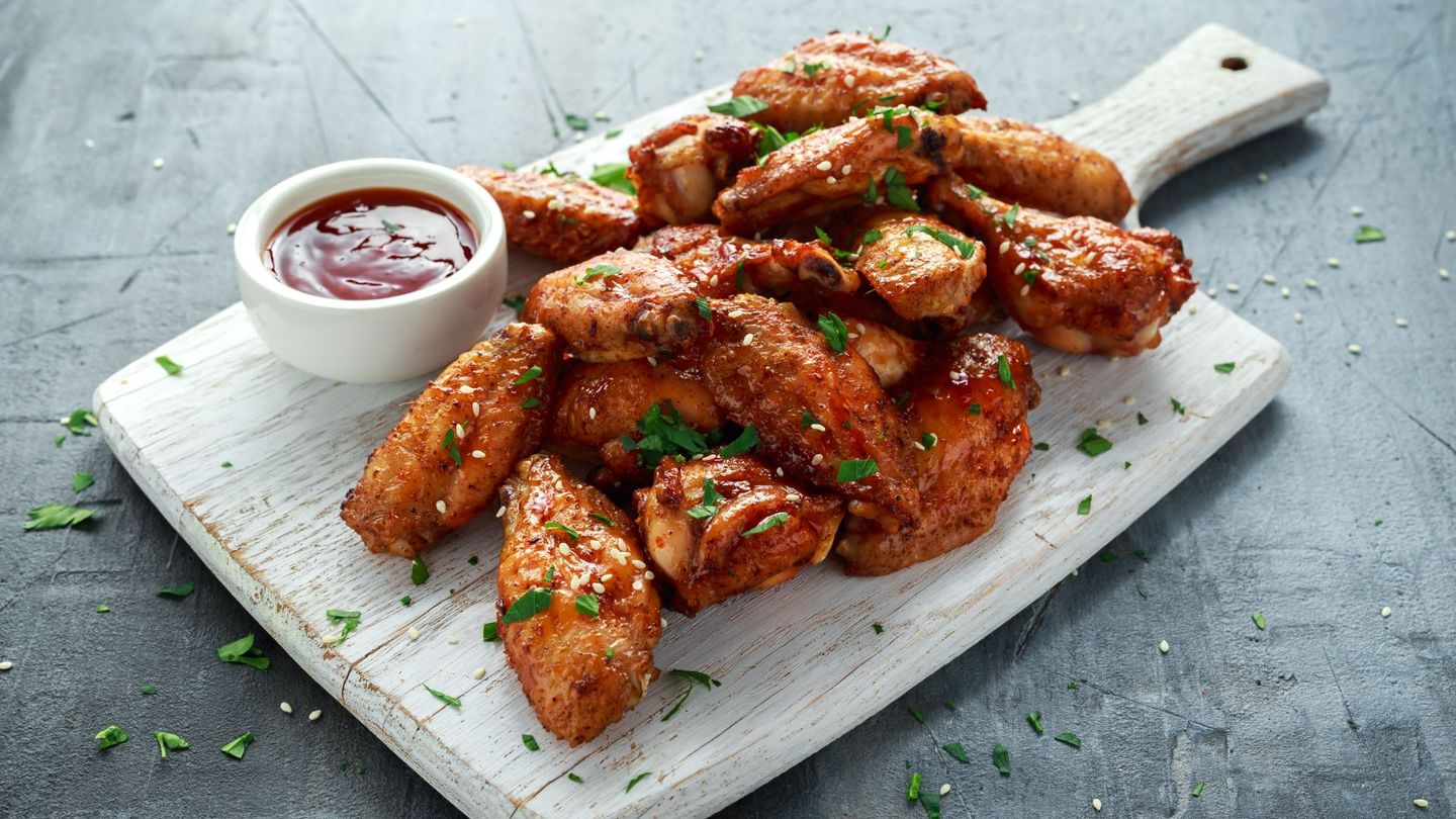 A cutting board topped with chicken wings and a bowl of ketchup.