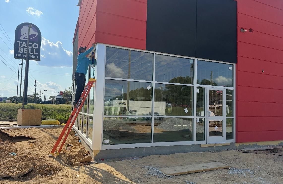 A person on a ladder working on the glass entrance of a Taco Bell restaurant under construction.