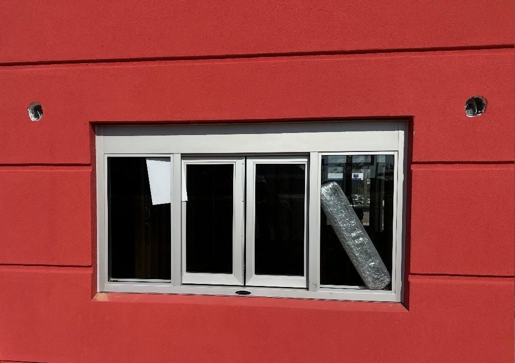 Red building exterior with a silver-framed window. A roll of grey material rests inside the window.
