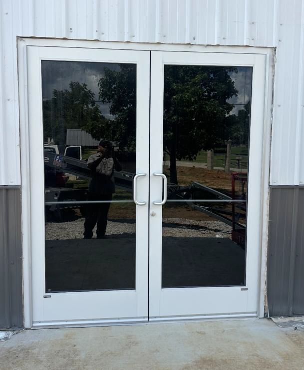 Double glass doors in a white frame, reflecting a person and trees.