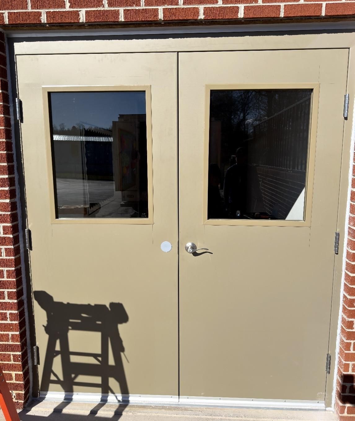 Tan double doors with windows, red brick building exterior, shadow of a sawhorse.