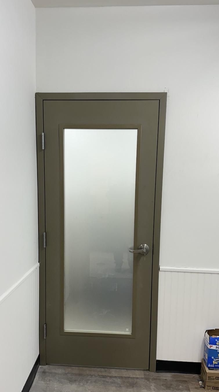 A gray door with a frosted glass panel set in a white wall corner.