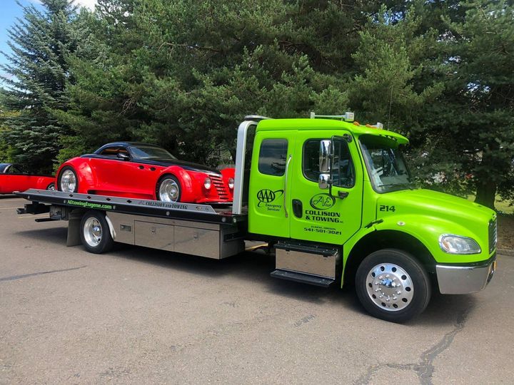 Bright green tow truck carrying a red sports car on a flatbed outdoors.