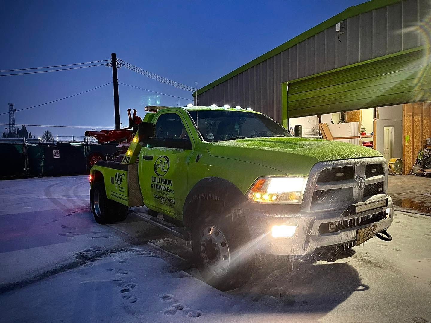 Bright lime-green tow truck in snowy lot beside a warehouse at dusk