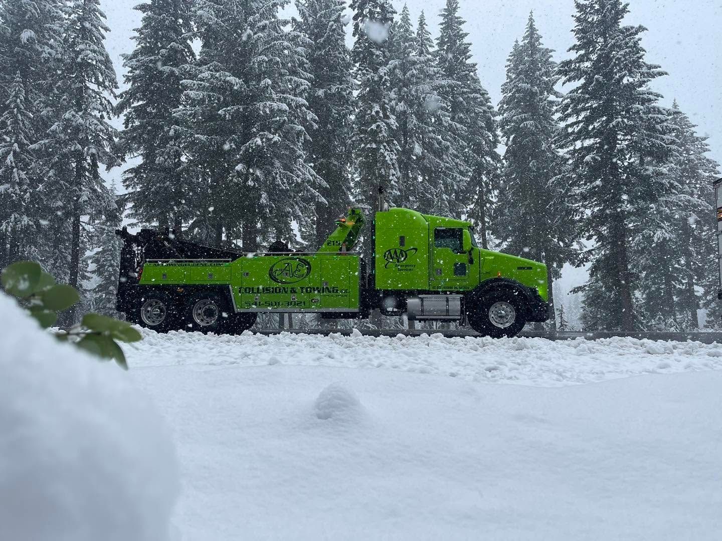 Bright green tow truck in snowy forest, parked on a snow-covered road.