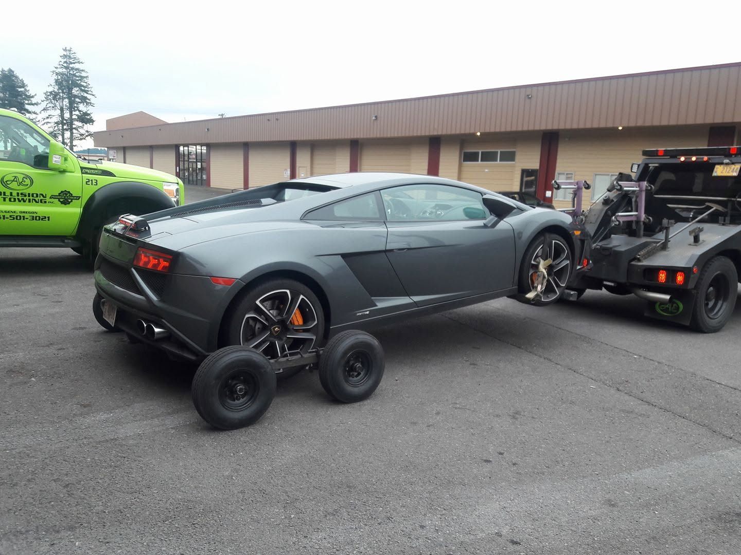 Gray sports car being towed on a dolly in a parking lot, with a lime green car nearby.