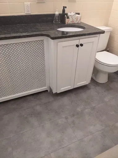Bathroom with white vanity, black countertop, toilet, and gray tiled floor.