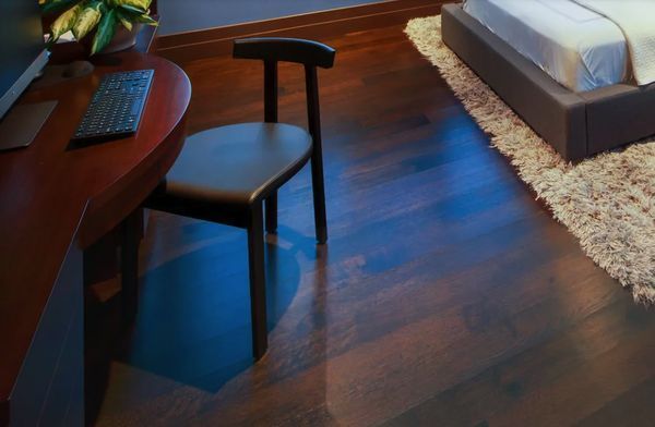 Dark wooden desk and chair in room with wooden floor, near a bed with shaggy rug.